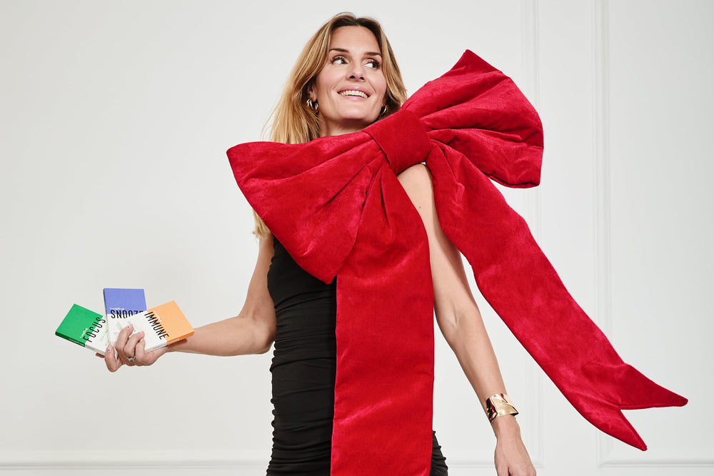 Woman wearing a black dress with a large red bow, holding boxes of Leapfrog IMMUNE, FOCUS and SNOOZE - natural supplements for immunity, stress and sleep