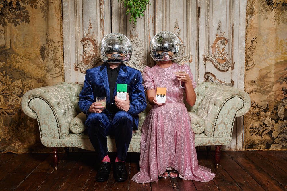 Two people sitting on an ornate couch with disco ball hats and Leapfrog IMMUNE and FOCUS natural supplements for anxiety, stress and immunity