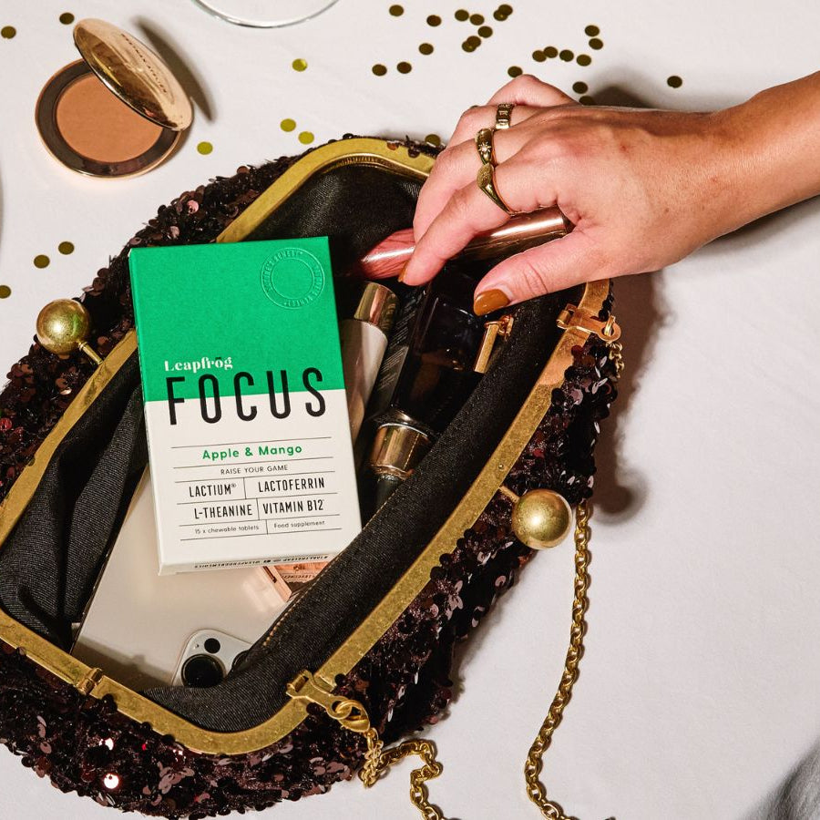 Hand reaching into a decorative handbag with a 'FOCUS' supplement for anxiety, next to a dessert on a pink plate.